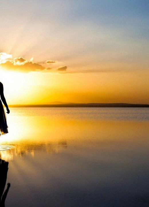 woman silhouette walking into calm water golden light