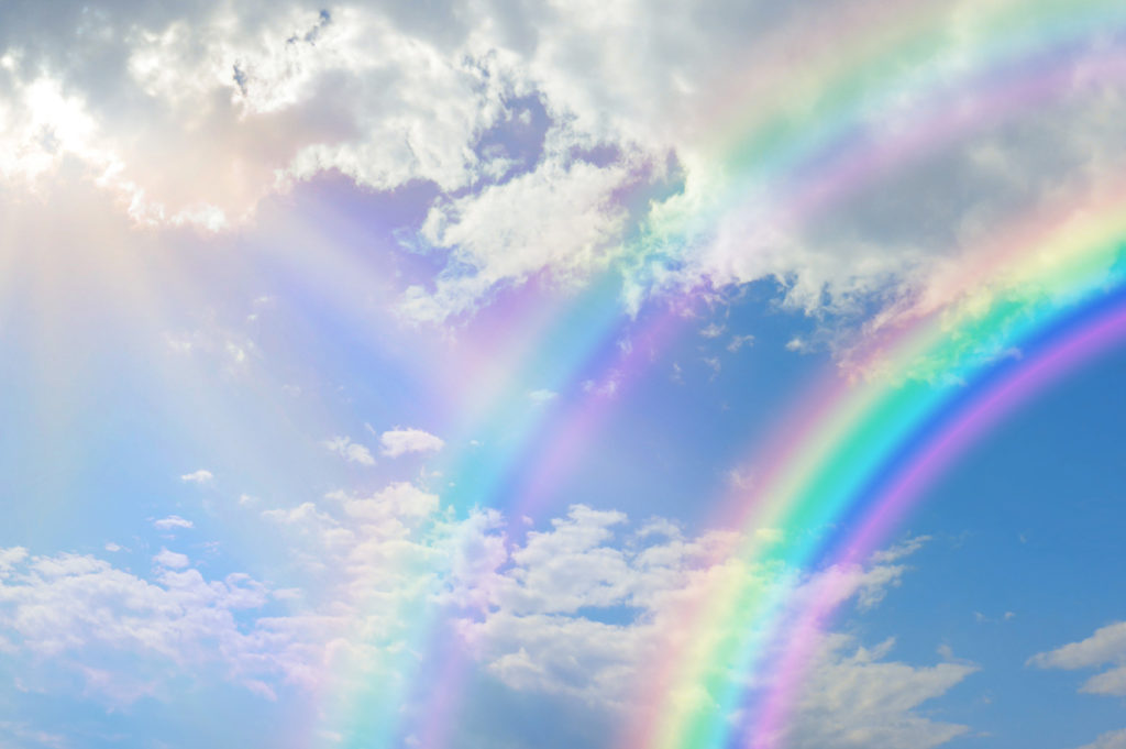 Beautiful vibrant double rainbow Cloudscape Background - awesome blue sky with pretty clouds, bright sun shining down and a large double rainbow arcing across the right corner with copy space